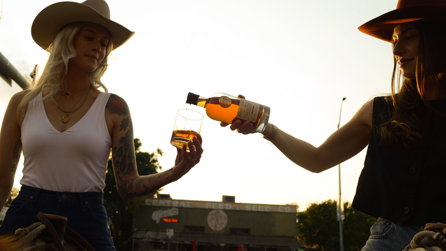 Two people in cowboy hats with drinks at an outdoor event.