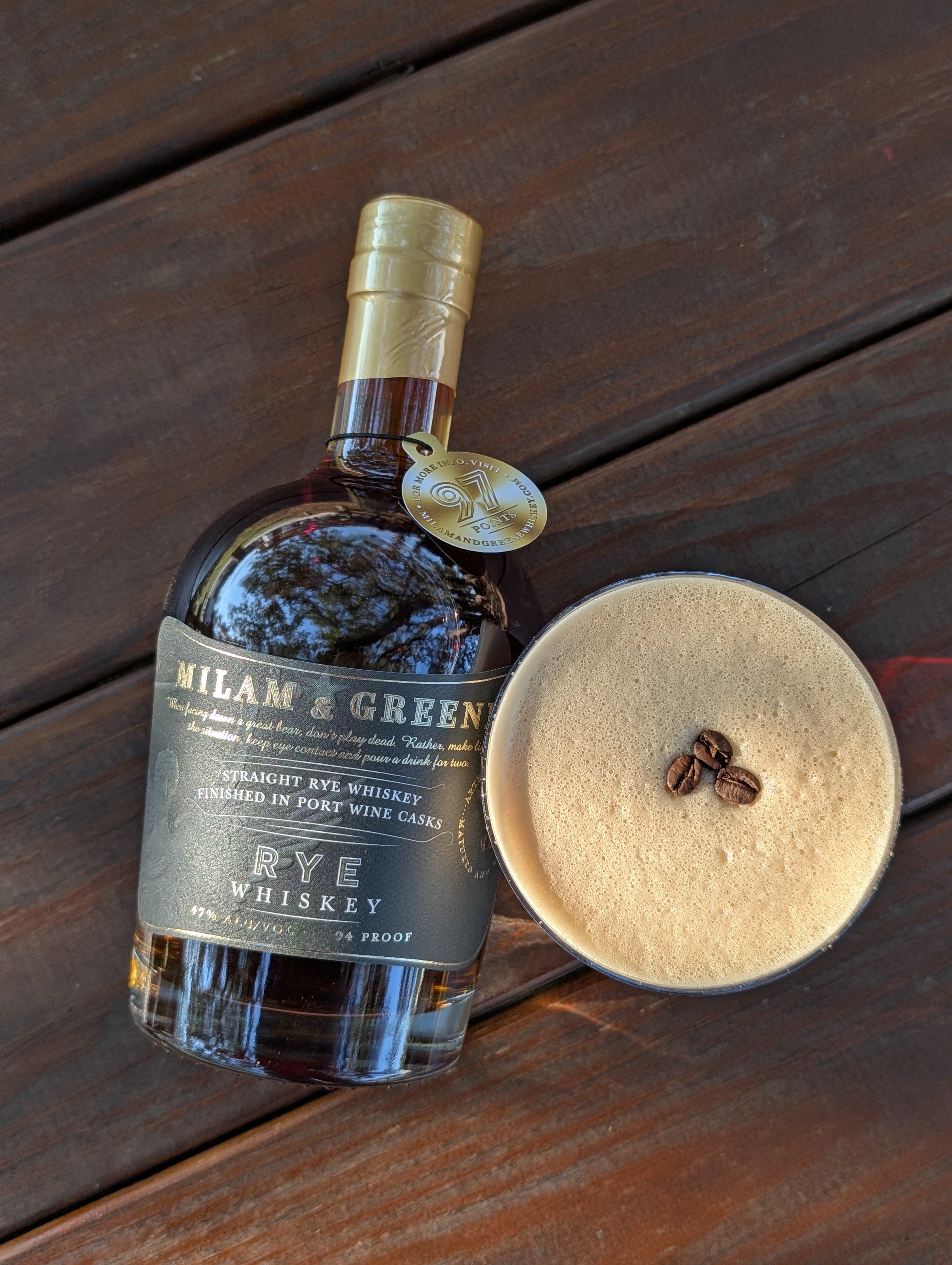Whiskey bottle on a table outside facing up to the sky with an overhead view of a coffee cocktail 