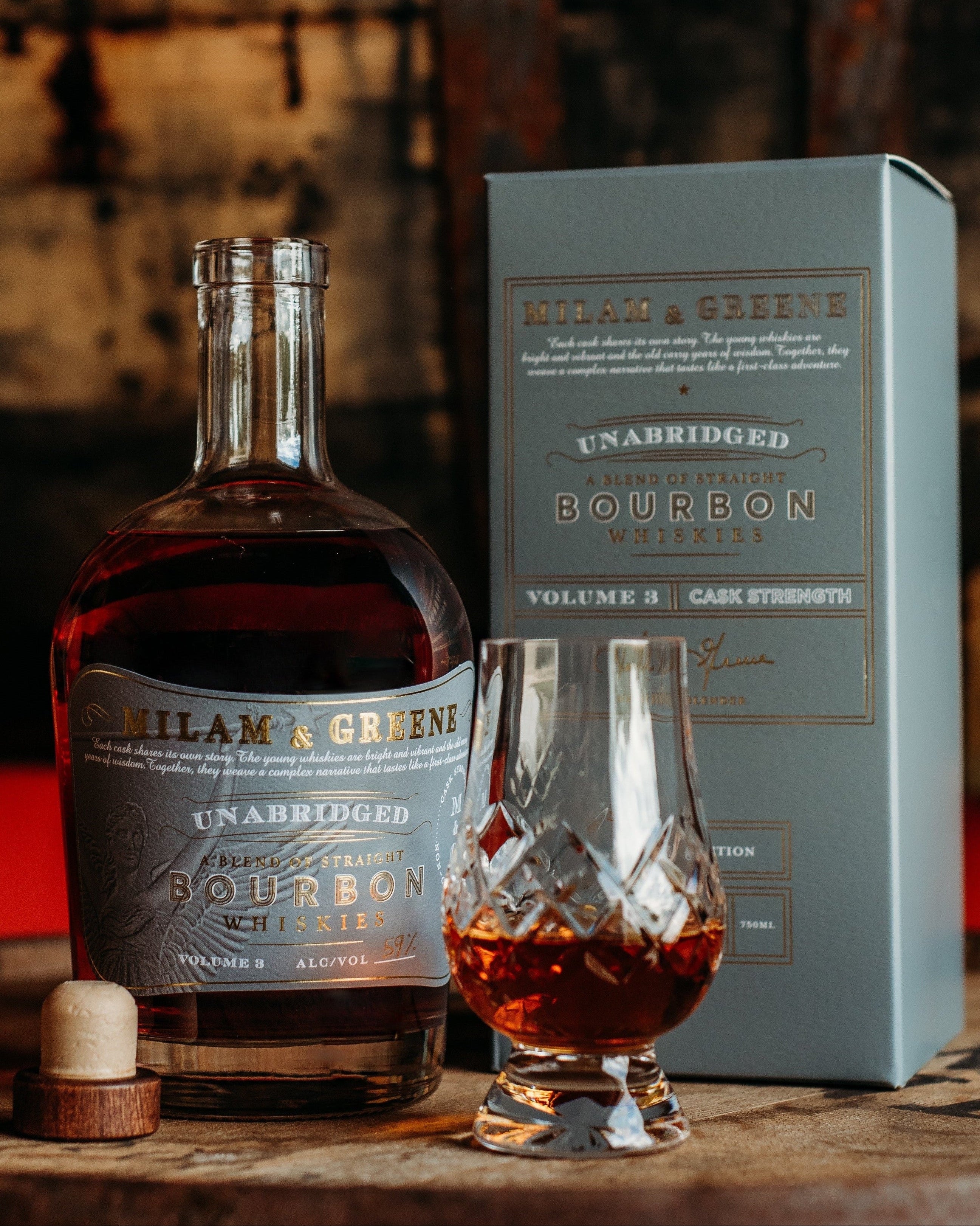 Bottle of Milam & Greene Unabridged Bourbon Vol 3 with a glass on a wooden barrel