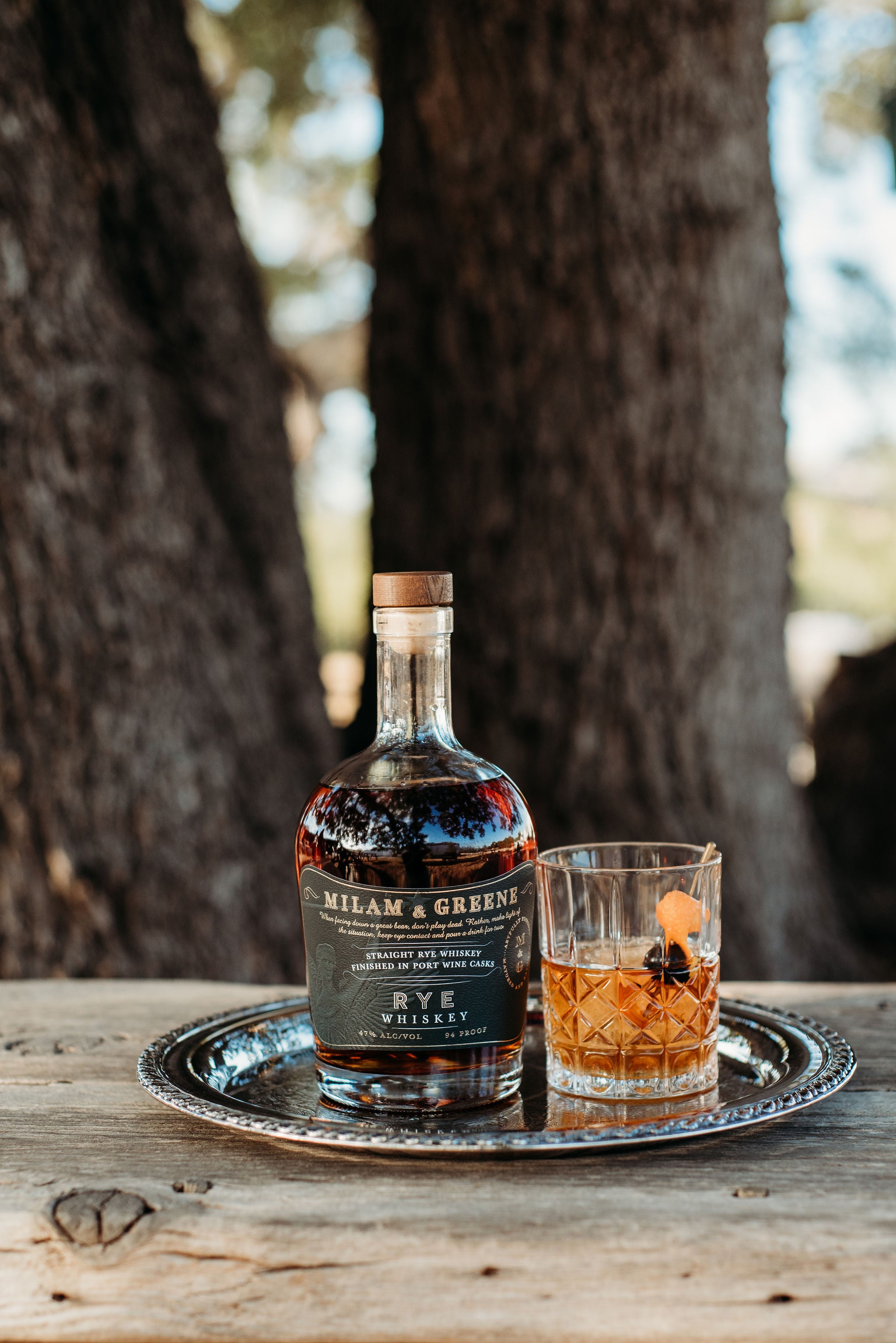 Bottle of Rye Whiskey with a glass on a wooden surface outdoors