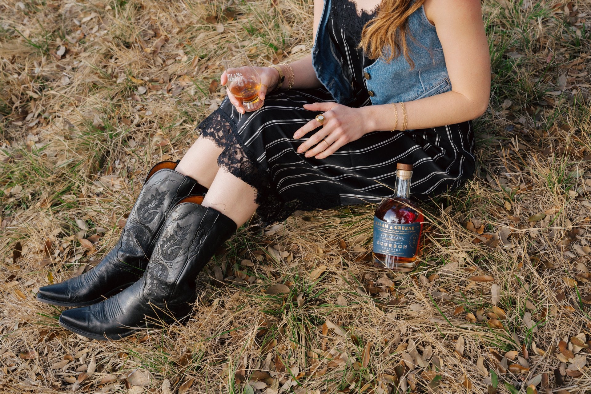 triple cask bourbon whiskey bottle lying in the grass next to some boots on a hillside